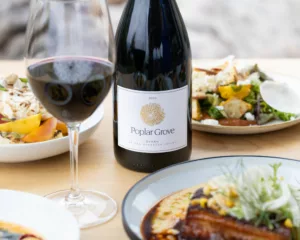 poplar grove bottle of Syrah and glass of wine on a table with restaurant food