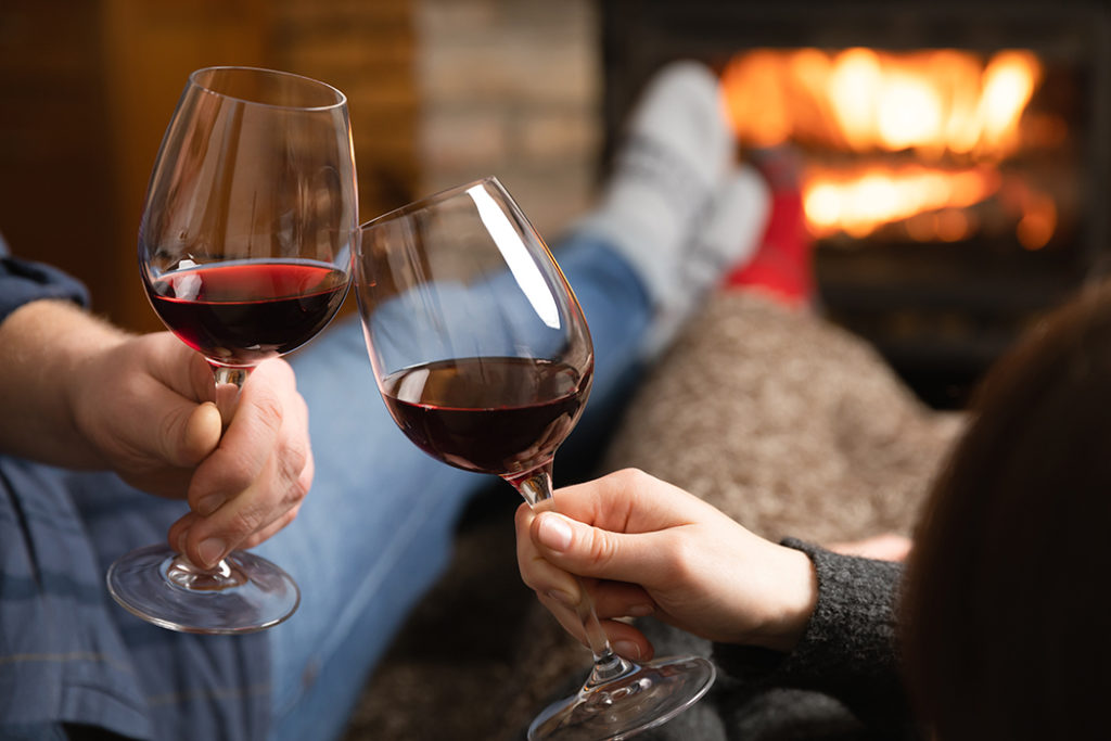 Couple in love sitting in a cozy room with fire place on a sofa - Wine Tour Hub - Wine Tour Hub cozy accommodations with fireplace and red wine